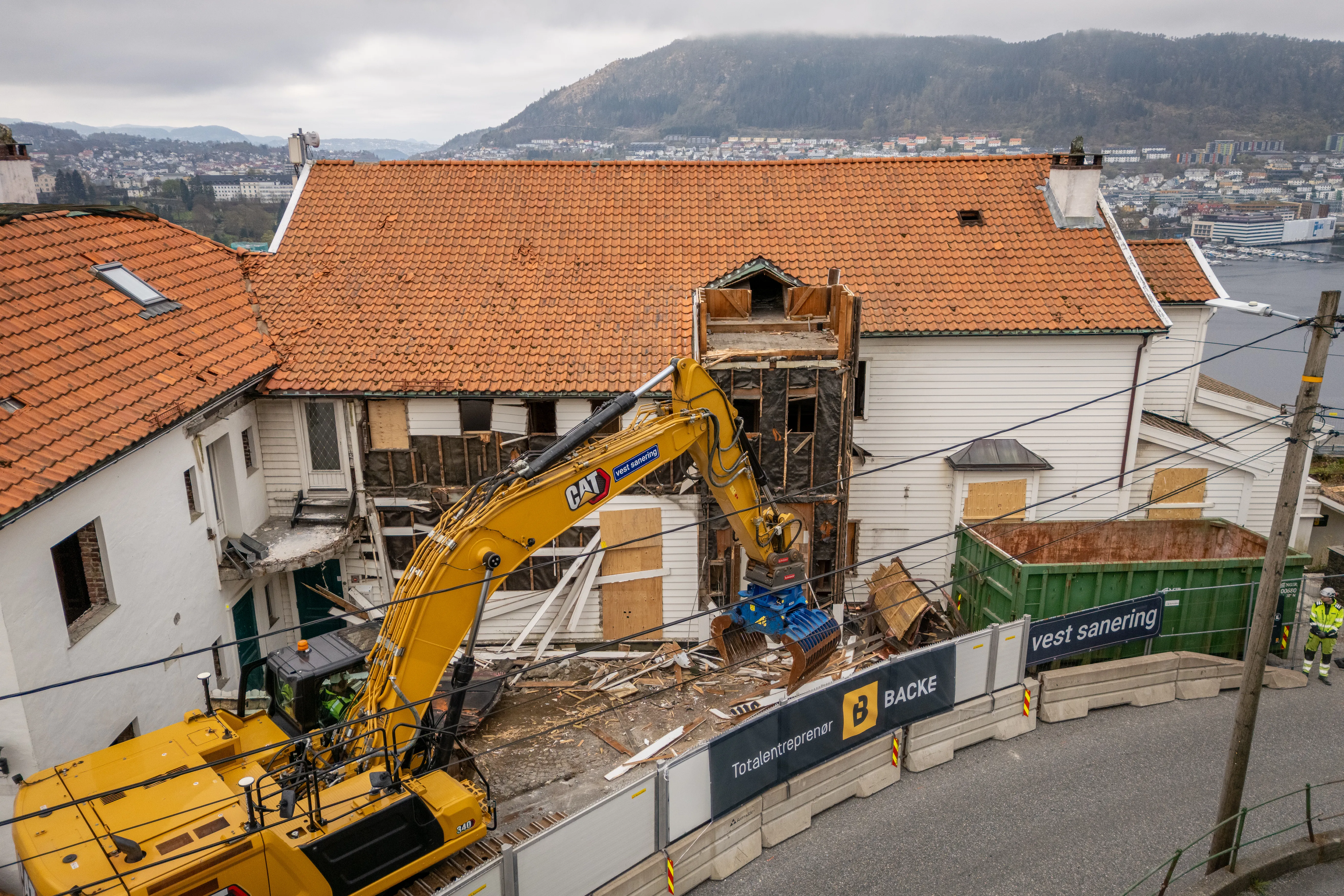 Gravemaskin river bygg på Bellevue i Bergen, med Vest Sanering-gjerde i forgrunnen